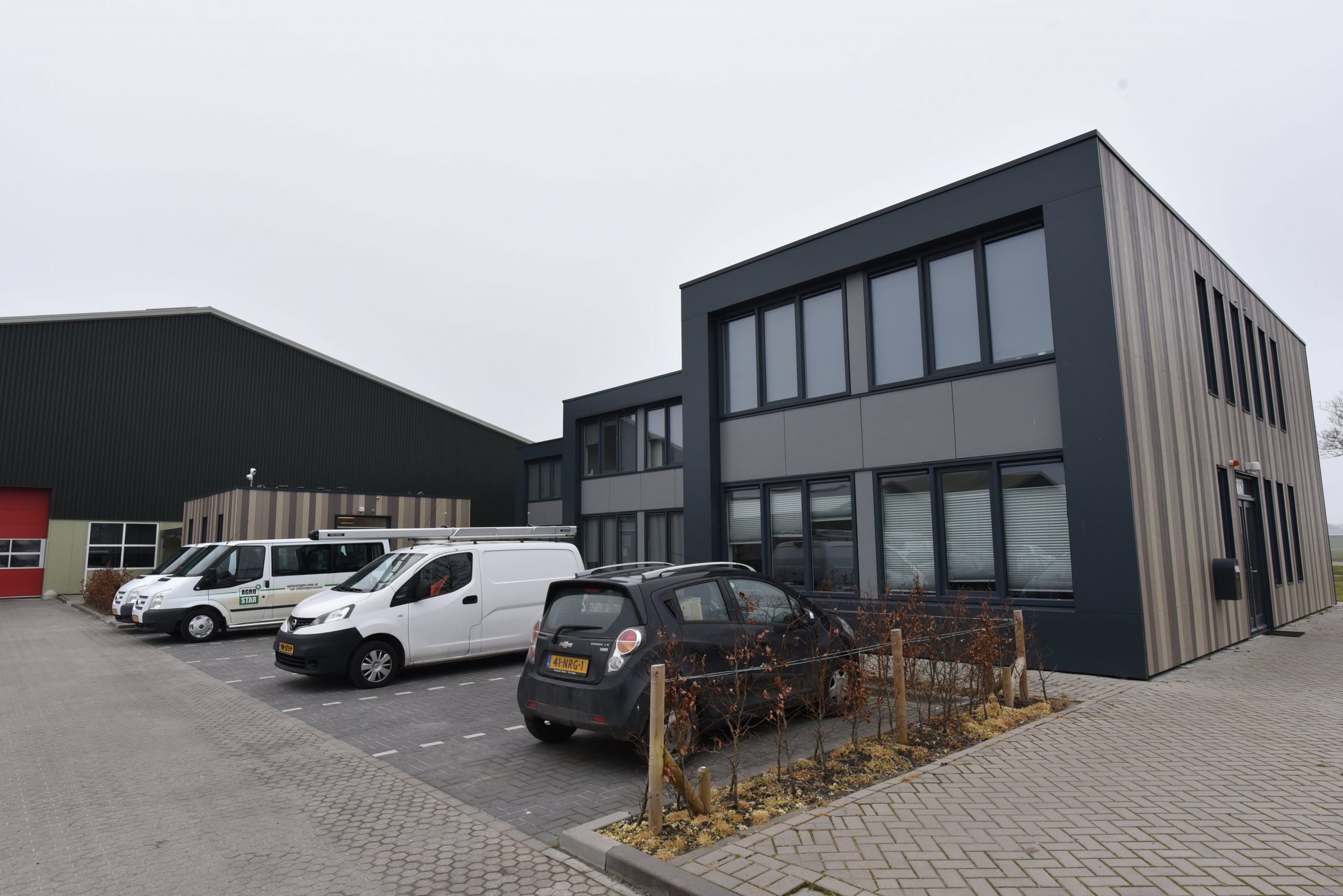 Twee verdiepingen met verticale Cedral-stroken in drie kleuren en een donkere kopgevel in 't Veld, met bedrijfsbussen op het parkeerterrein